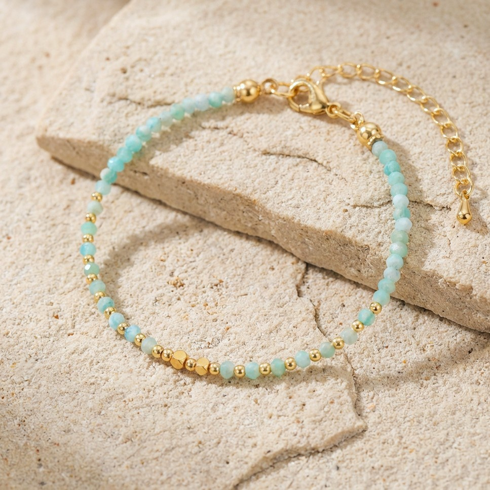 Bracelet with gold and faceted light blue aquamarine gemstone beads on a beige stone surface