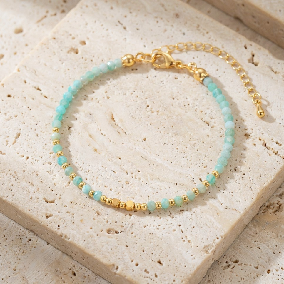 Dainty bracelet with faceted blue aquamarine gemstone beads and gold accents on a beige stone surface