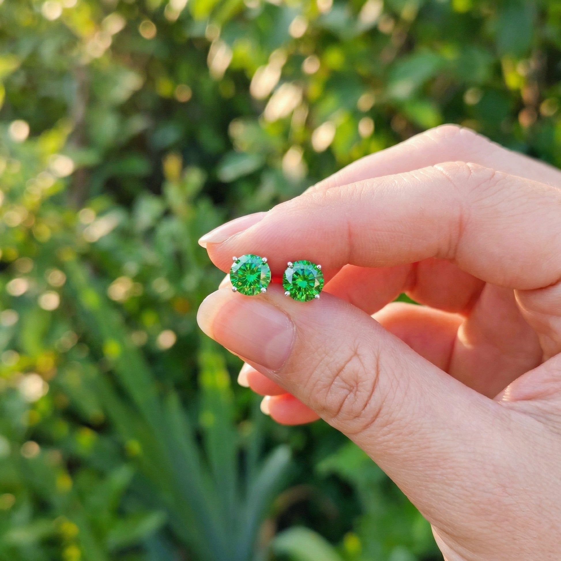 A hand holding 925 Sterling silver stud earrings with bright emerald green crystals