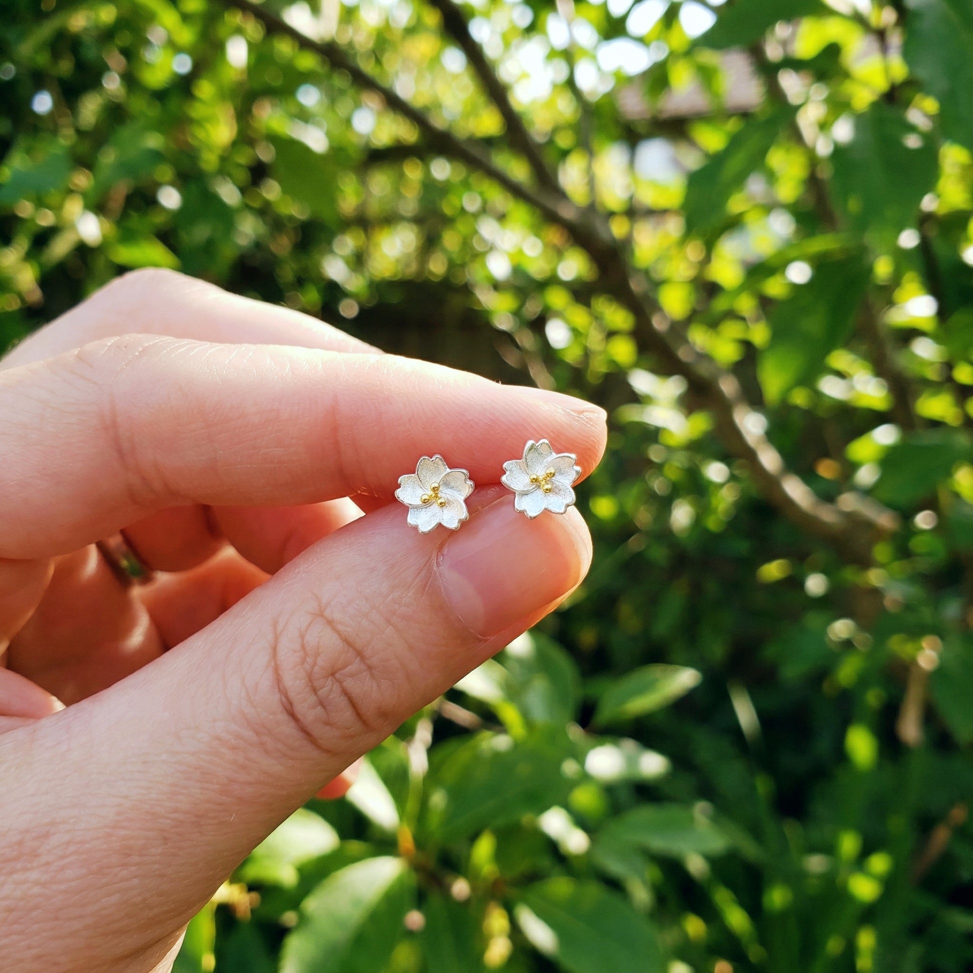 Flower-shaped earrings held between fingers with a green leafy background