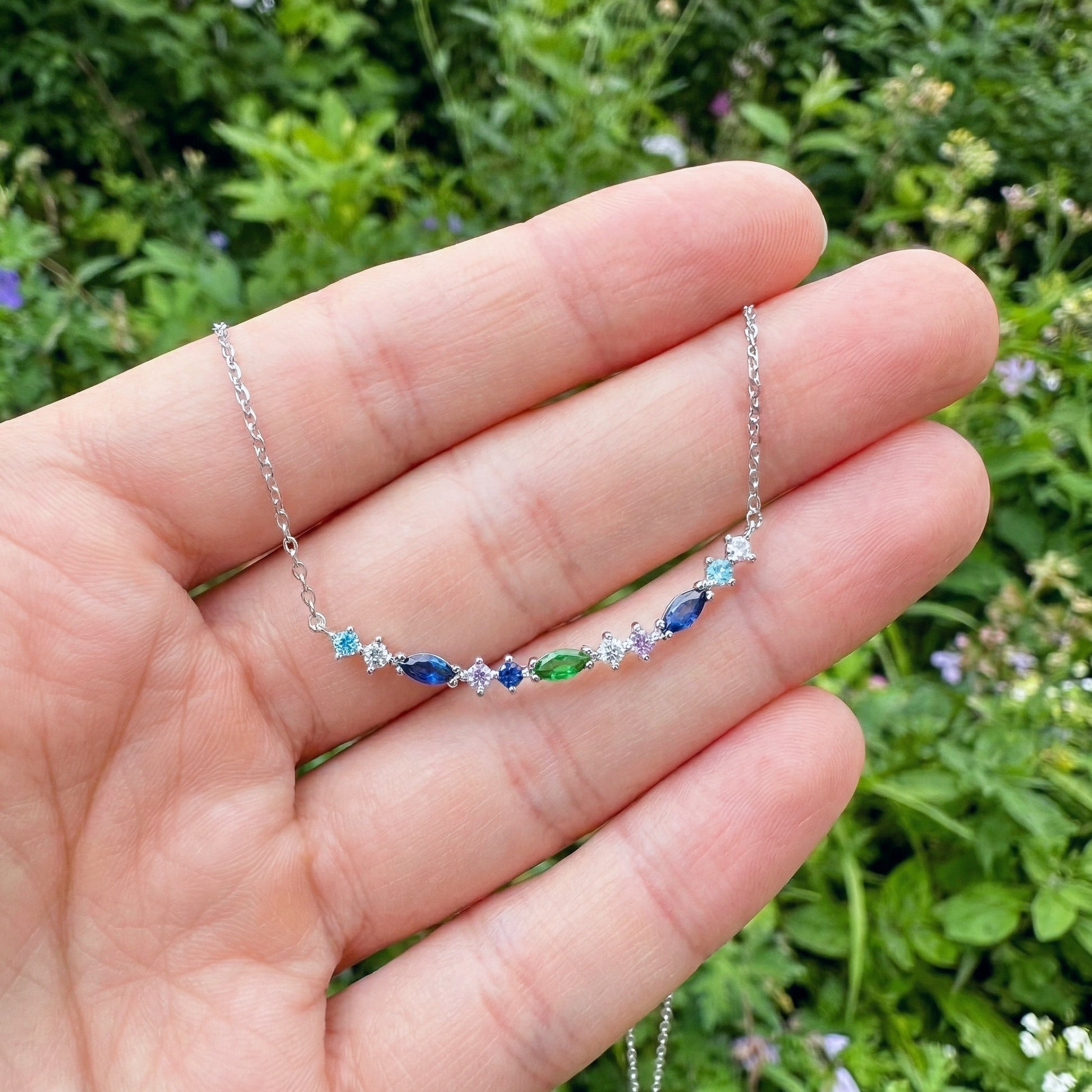 Silver necklace with colorful stones held in a hand against a green background