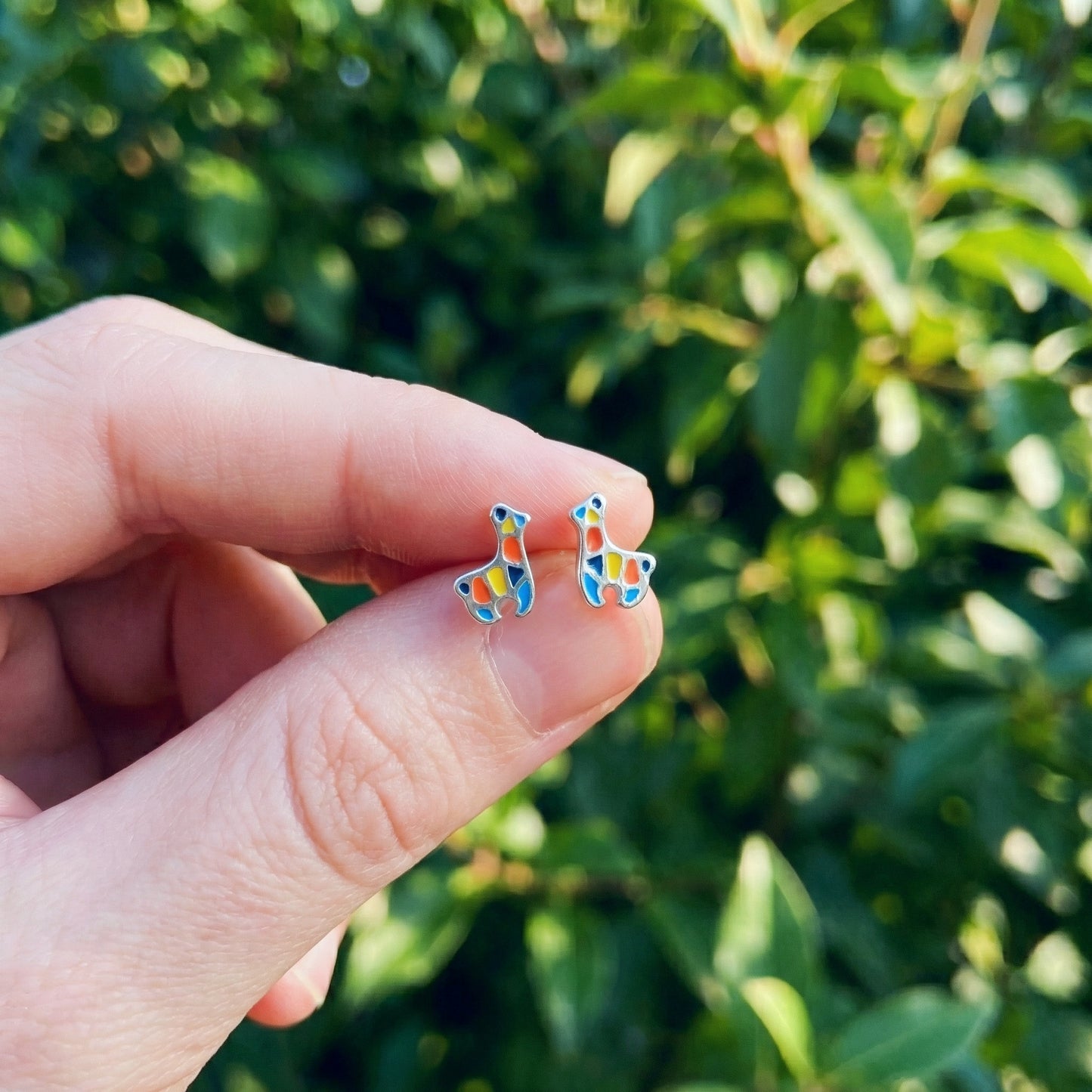 Hand holding colorful llama earrings with a green leafy background