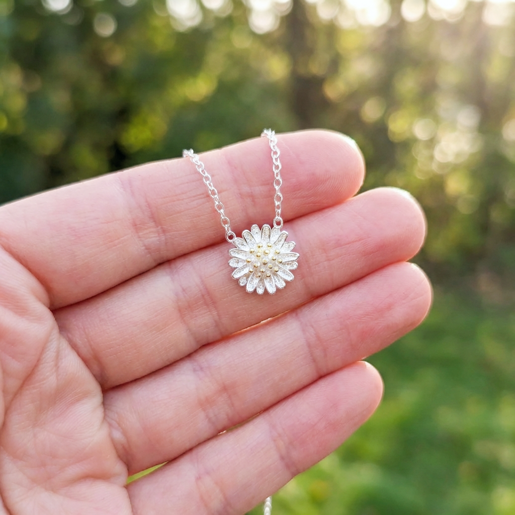 Silver necklace with a daisy pendant held in a hand against a blurred green background