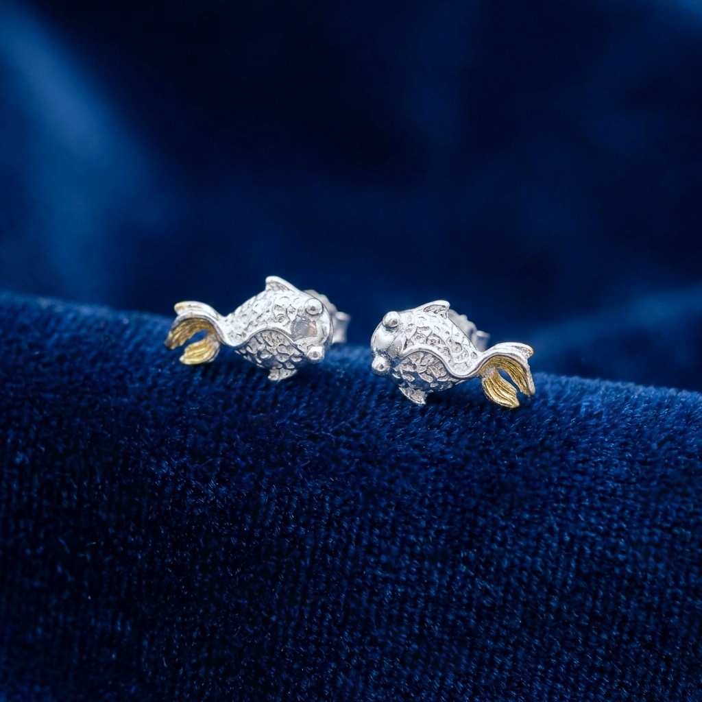 Silver fish stud earrings with gold tails on a blue background