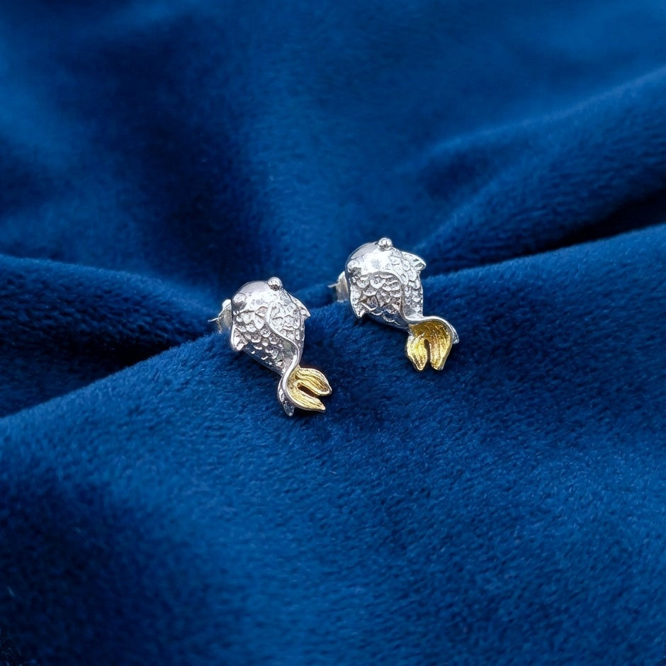 Silver fish stud earrings with gold tails on a blue background