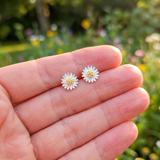 A hand holding little daisy silver stud earrings 