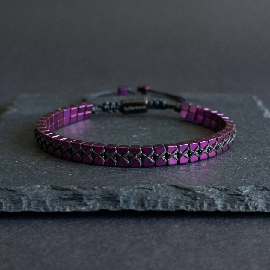 A men's hematite bracelet with mtallic purple cube beads woven together and an adjustable bolo cord, on a dark background