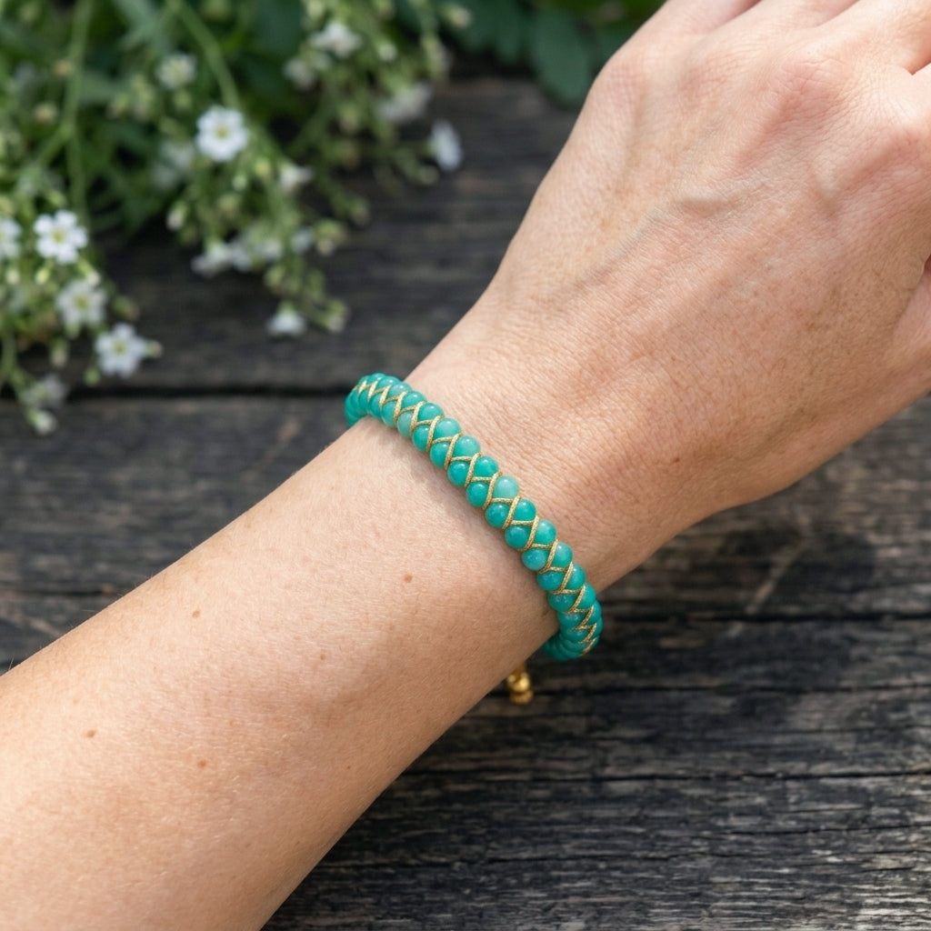 Turquoise braided Amazonite gemstone bracelet on a woman's wrist with a wooden background and flowers.