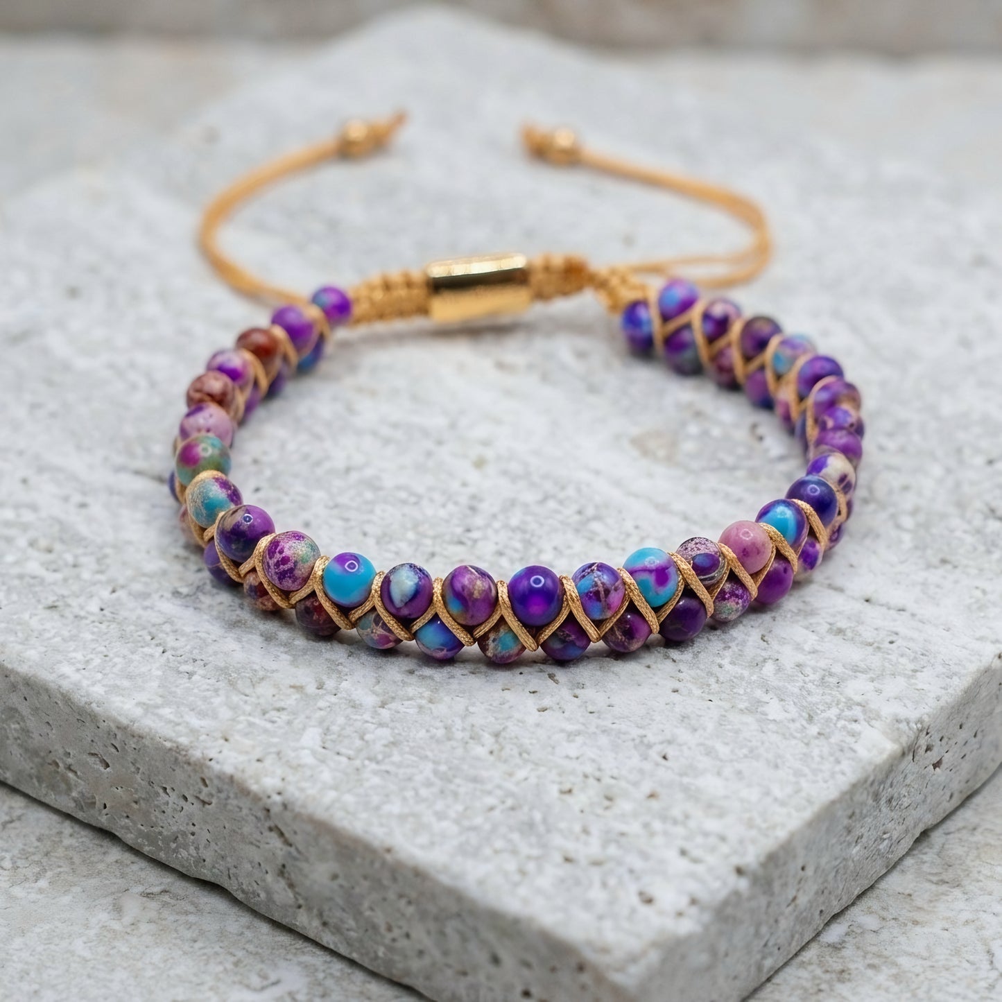 Galaxy sea sediment jasper bead bracelet on a stone surface. The colorful purple and blue gemstone beads are woven into a double row with an adjustable drawstring clasp.