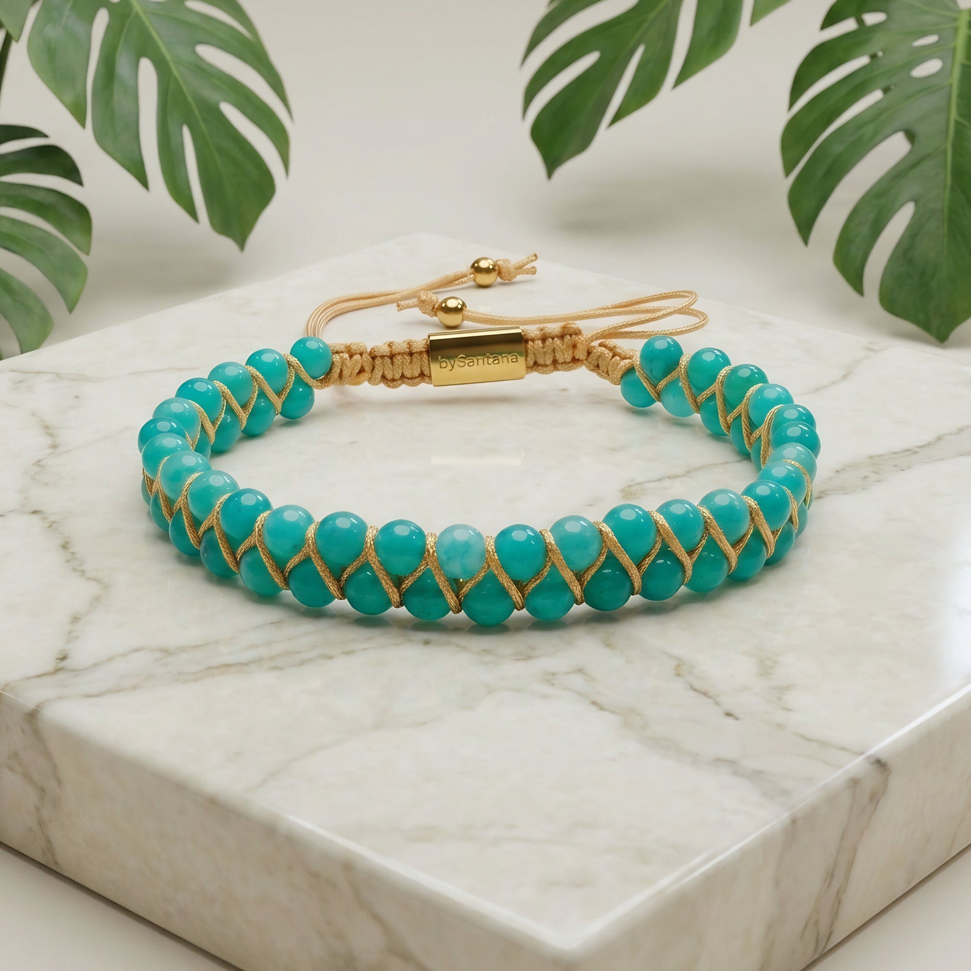 Turquoise beaded bracelet with Amazonite beads and gold accents on a marble surface with green leaves in the background