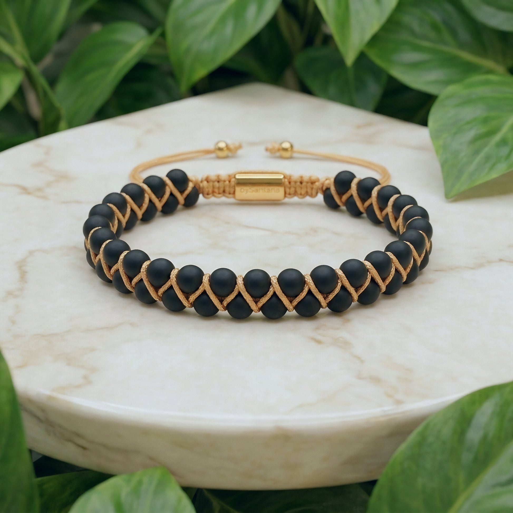 Matt Black Onyx beaded gemstone bracelet with gold accents on a marble surface with green leaves in the background