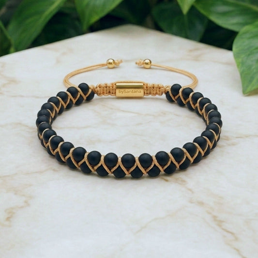 Matt Black Onyx beaded gemstone bracelet with gold accents on a marble surface with green leaves in the background