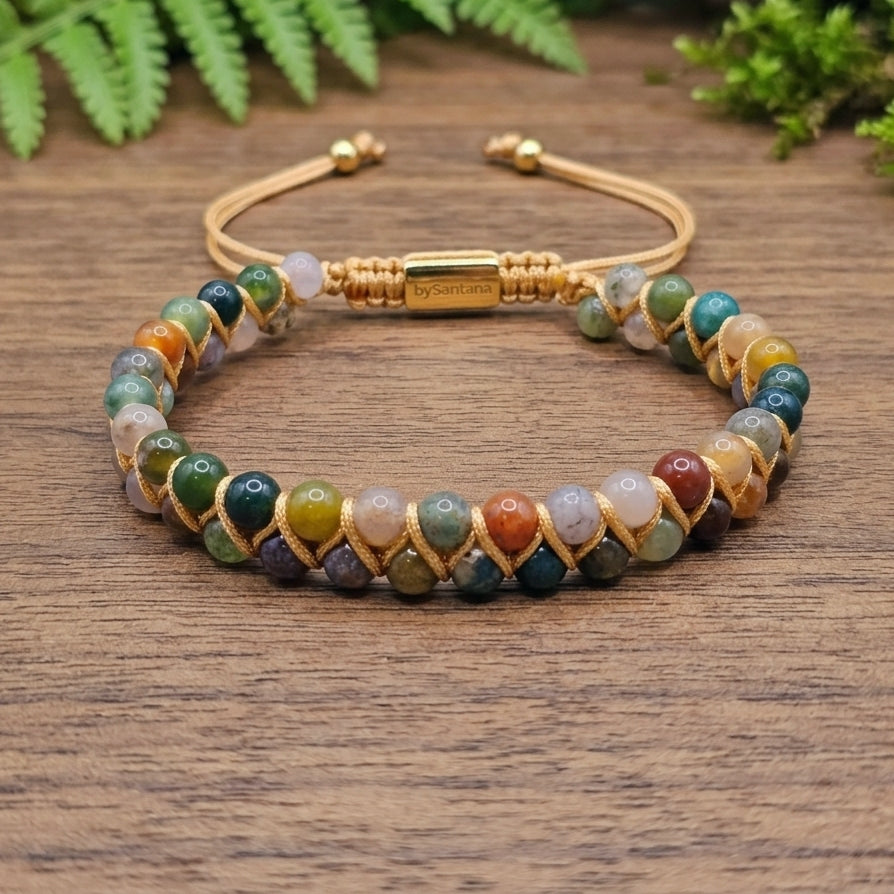 Multicolored beaded bracelet with gold clasp on a wooden surface with green foliage in the background
