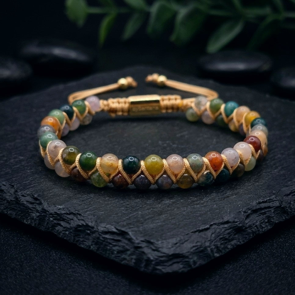 Multicolored beaded bracelet with Indian Agate gemstone beads and gold cord wrapping on a dark stone surface with greenery in the background