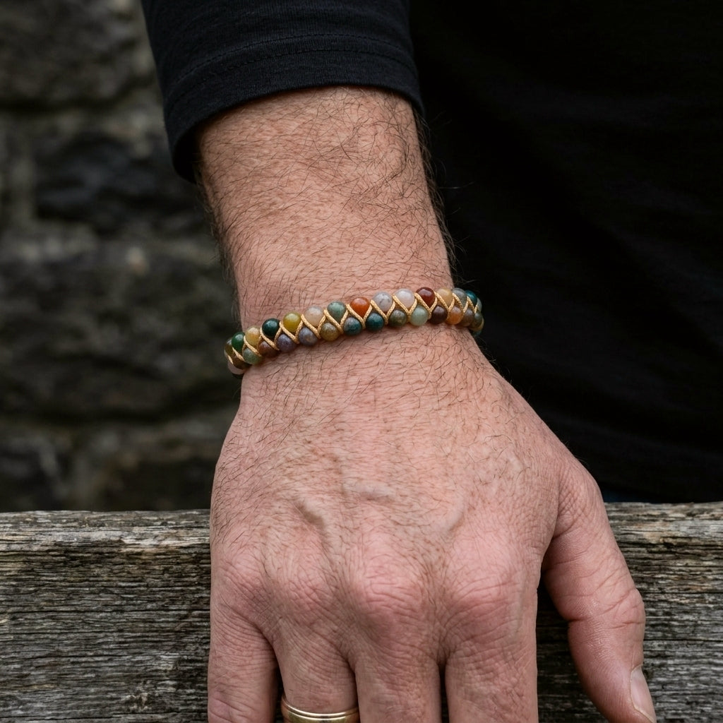 A man's hand wearing a earthy colour beaded bracelet with a stone wall background