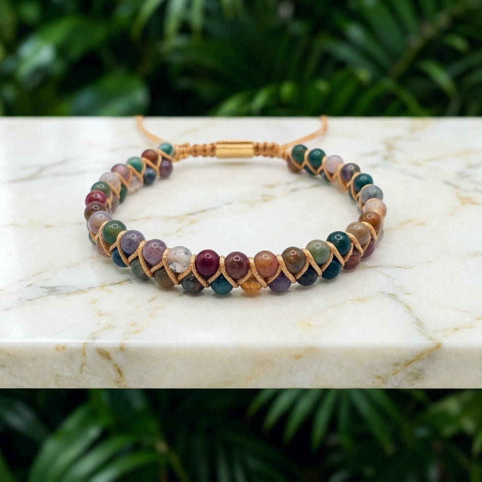 Colourful Indian Agate beaded bracelet with a double row of earthy brown yellow orange and white gemstone beads, woven together with an adjustable bolo clasp, on a marble background with greenery.