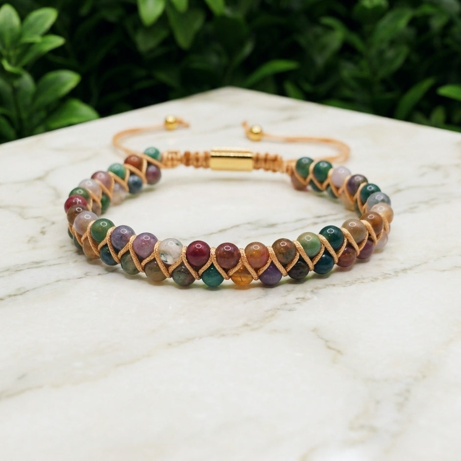 Colourful Indian Agate beaded bracelet with a double row of earthy brown yellow orange and white gemstone beads, woven together with an adjustable bolo clasp, on a marble background with greenery.