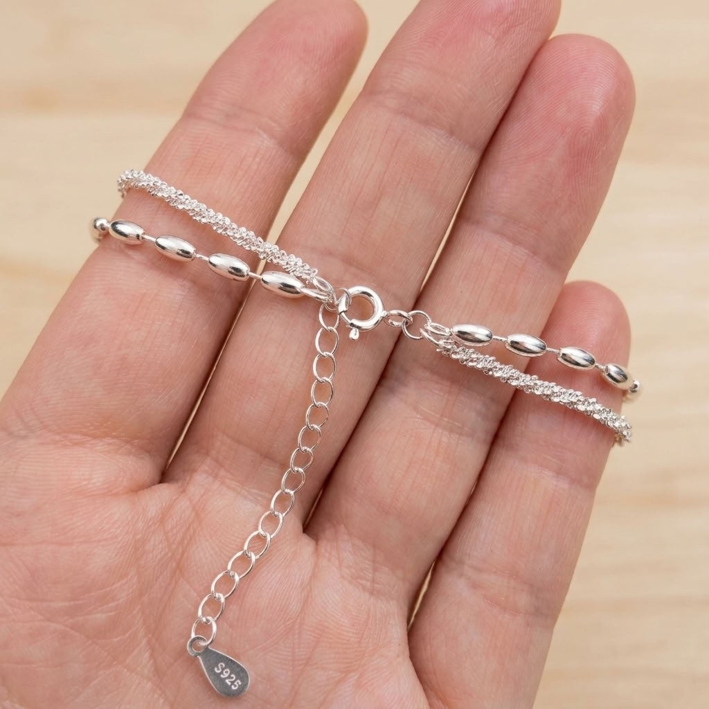 A silver chain bracelet with textured and smooth links, displayed on a person's hand. The bracelet features a lobster clasp and an adjustable extension chain with a small '925' sterling silver tag.