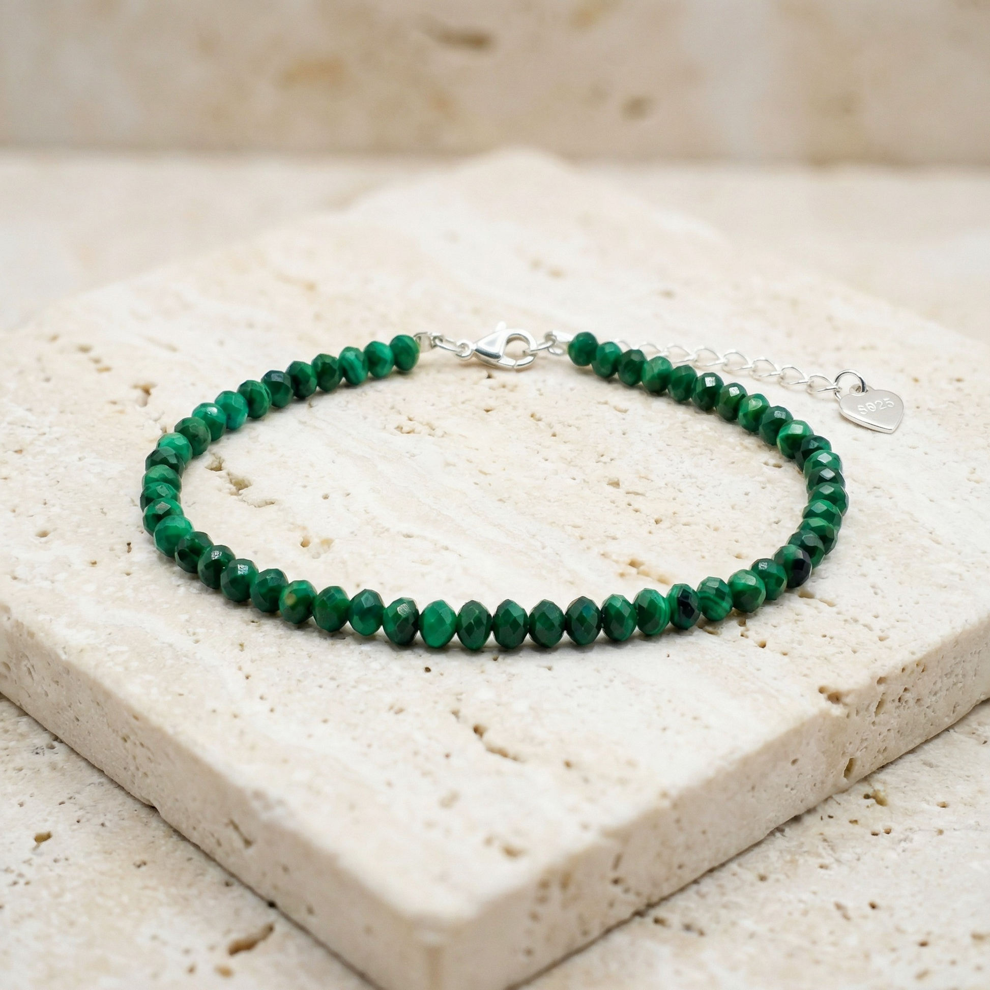 Natural green malachite bead bracelet with a 925 silver clasp on a light stone background