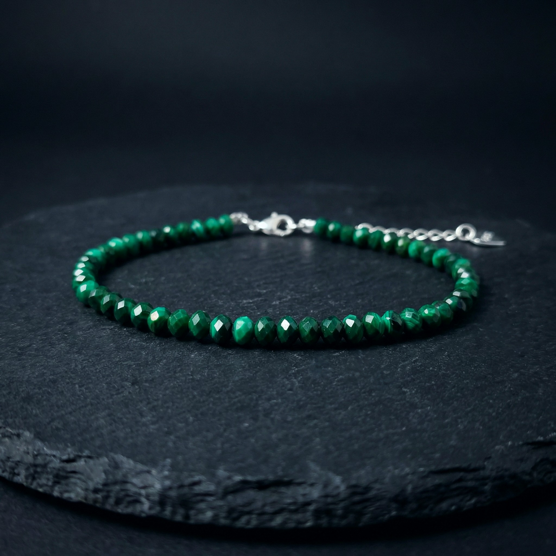 Natural green malachite bead bracelet with a 925 silver clasp on a dark stone background