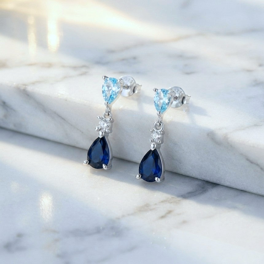 Pair of dainty silver earrings with blue gemstones on a marble surface