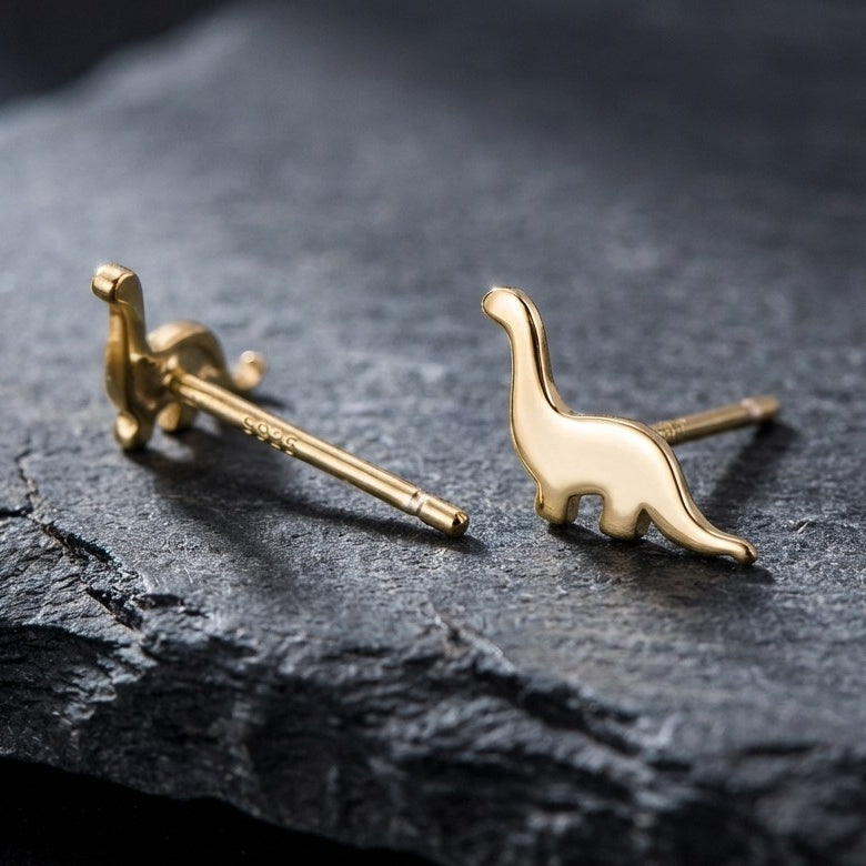 Gold dinosaur-shaped earrings on a dark stone surface