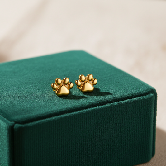 Gold paw print stud earrings on a green jewelry box