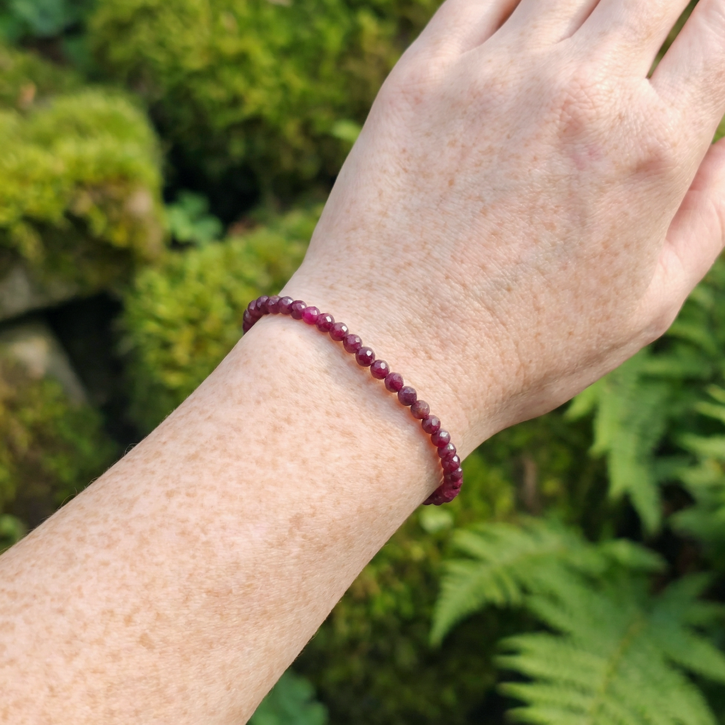 Hand wearing a red ruby beaded bracelet with a green natural background