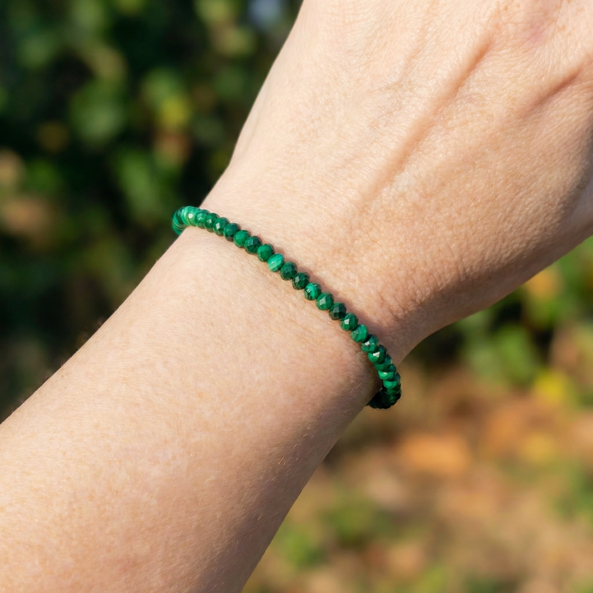 an arm wearing a natural green malachite bead bracelet with a 925 silver clasp outside in the sun
