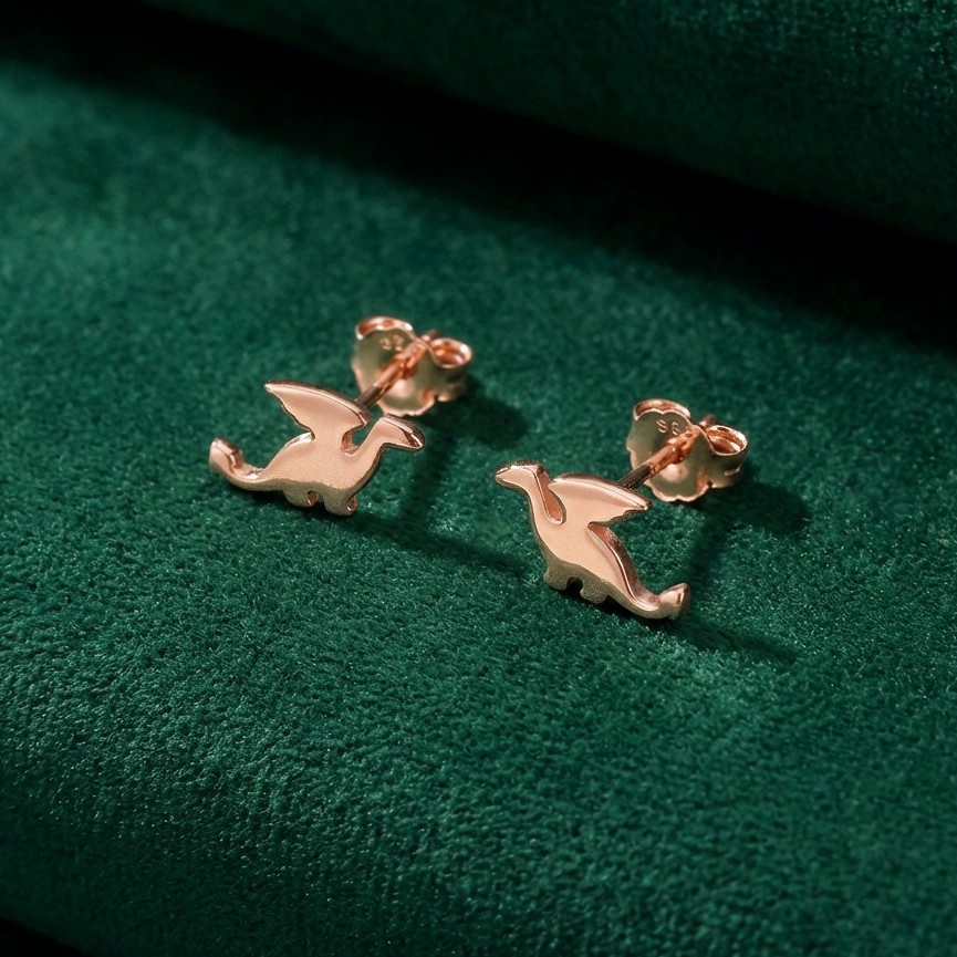 Rose gold dragon-shaped earrings on a green fabric background