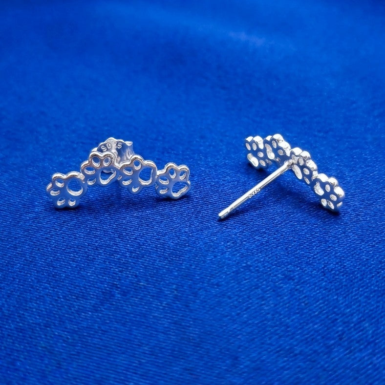 Silver paw print earrings on a blue background. the earrings have 925 on them