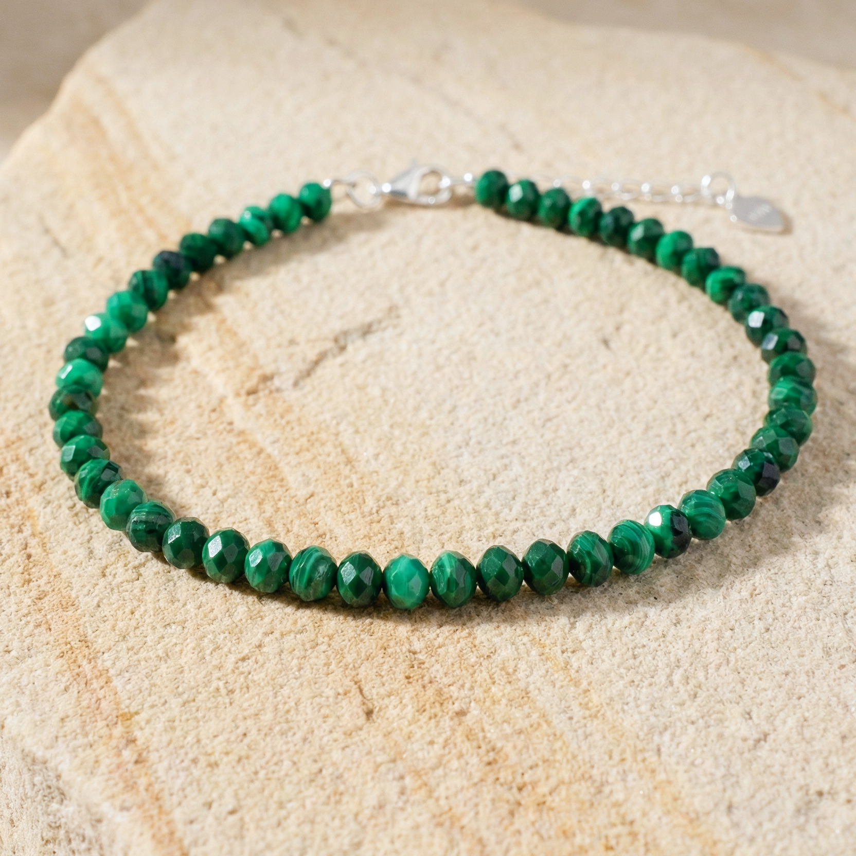 Natural green malachite bead bracelet with a 925 silver clasp on a light stone background