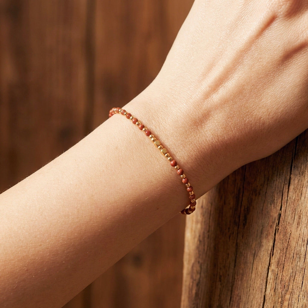 A wrist with a dainty bead bracelet with gold sandstone gemstone beads. 
