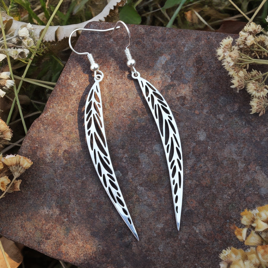 Long pointy stainless steel leaf earrings with silver hooks on a stone background 
