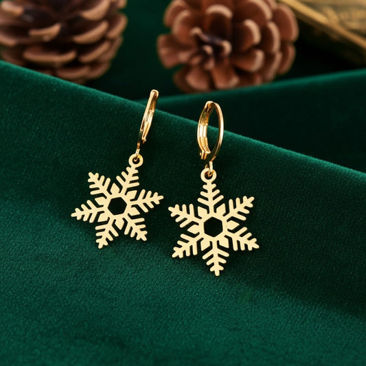 Gold snowflake earrings with hoops on a green fabric background with pine cones.
