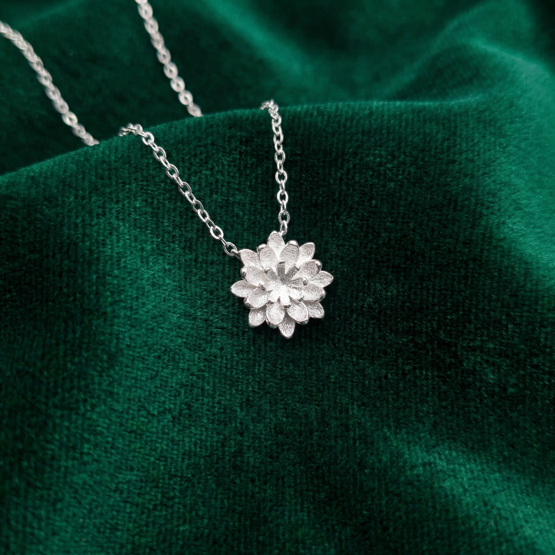 Silver lotus flower pendant necklace on a green fabric background