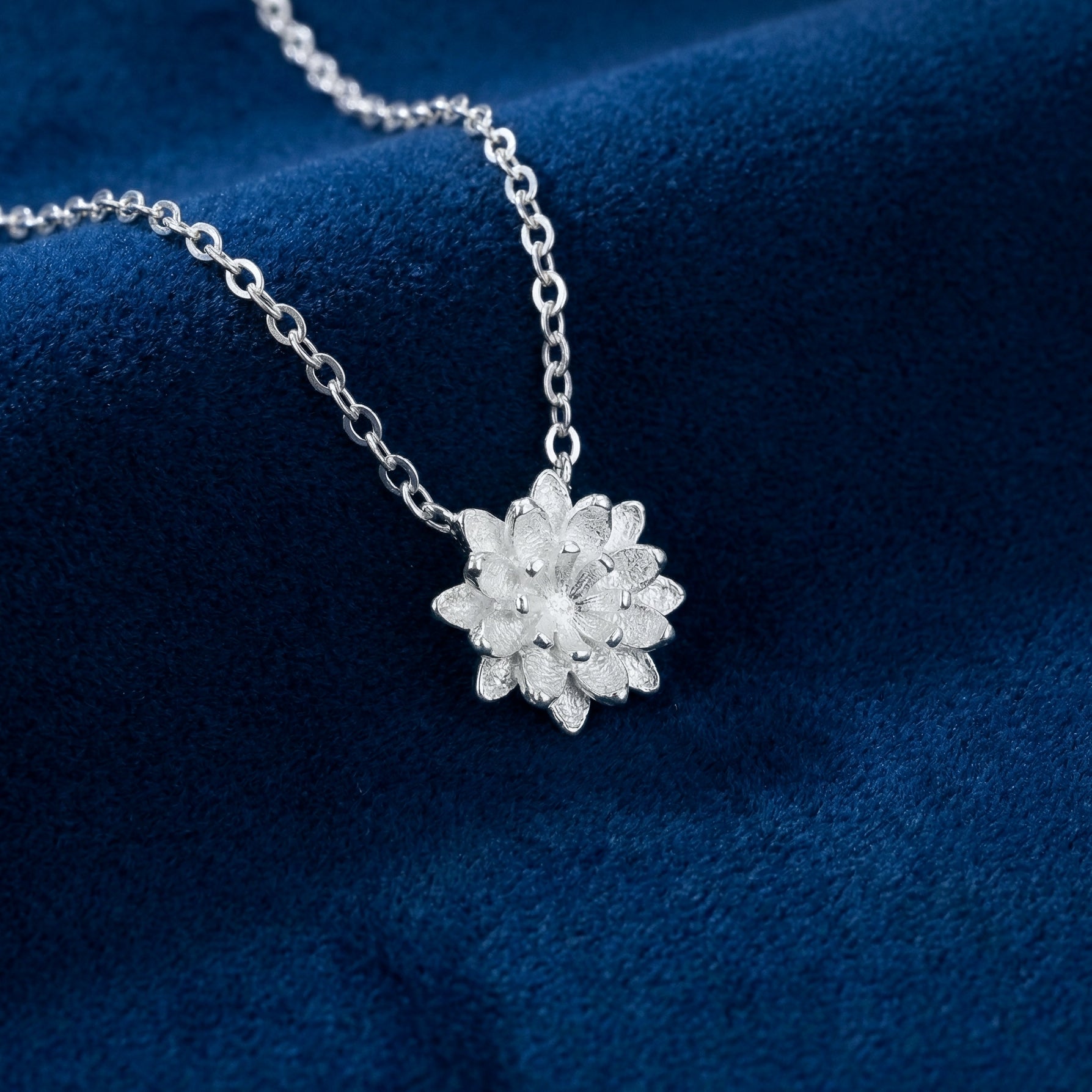 Silver necklace with a flower pendant on a blue fabric background