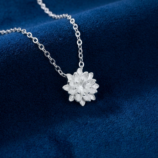 Silver necklace with a flower pendant on a blue fabric background