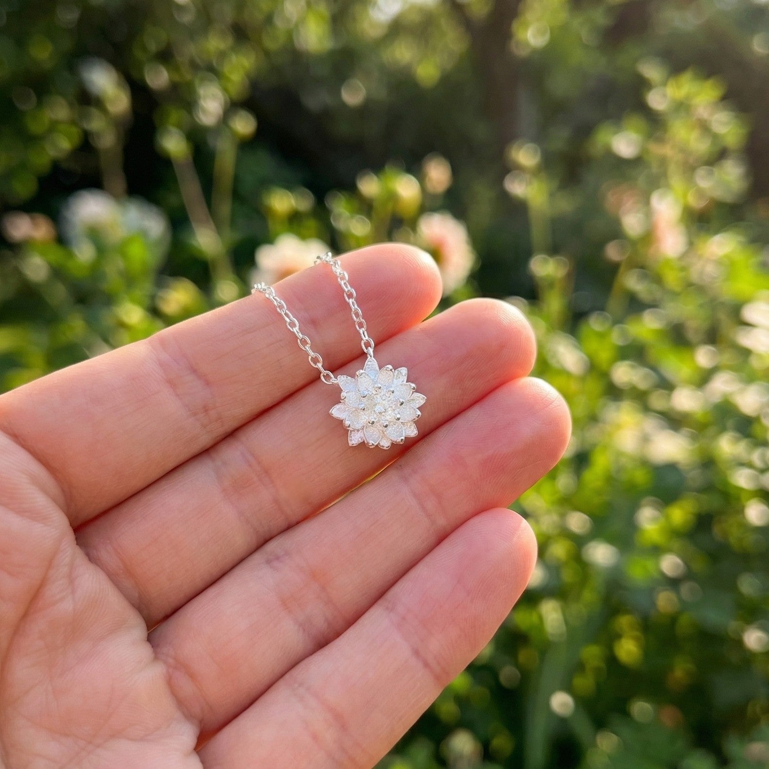 Silver necklace with a floral pendant held in a hand against a blurred green background