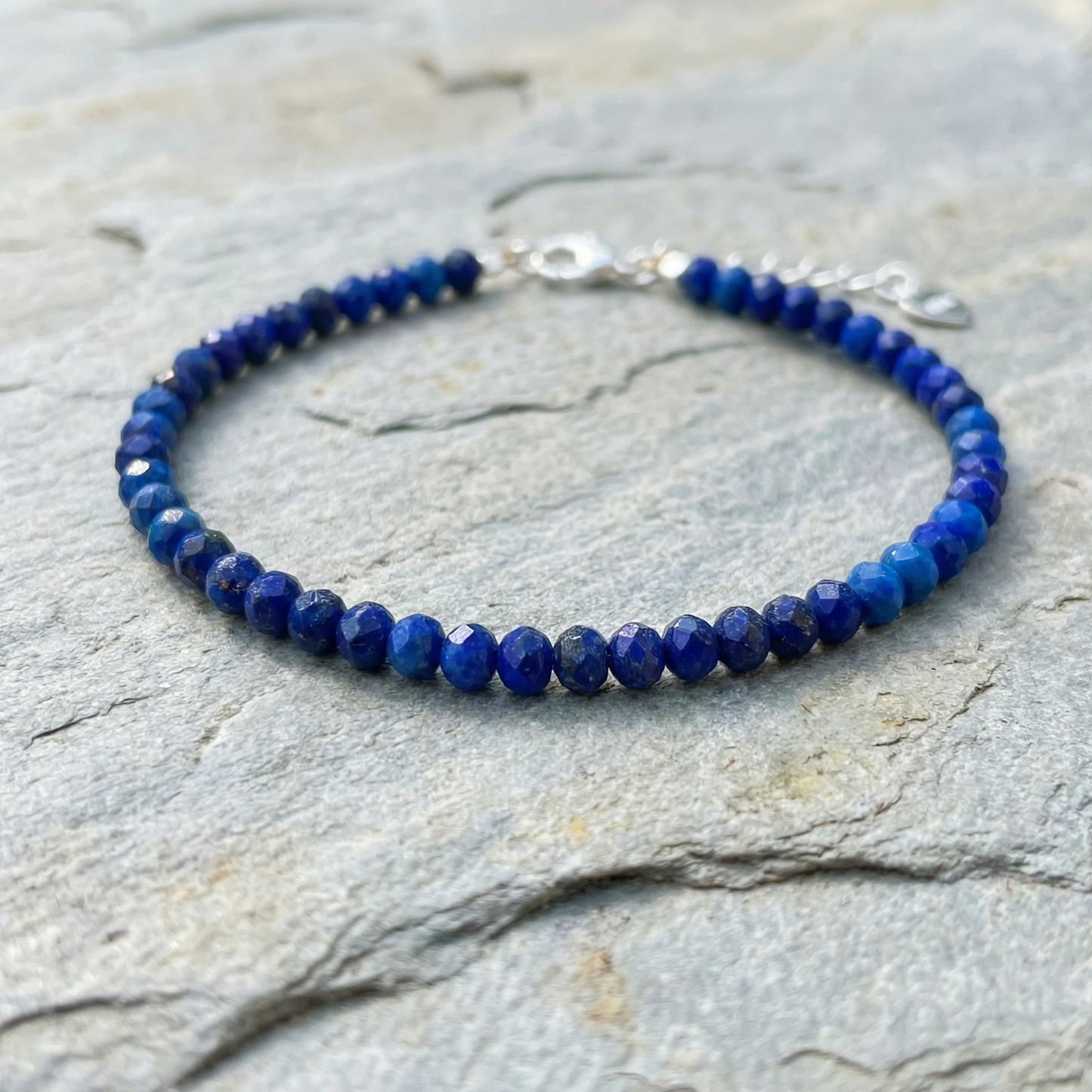 Blue lapis lazuli beaded bracelet with 925 silver clasp on a stone surface