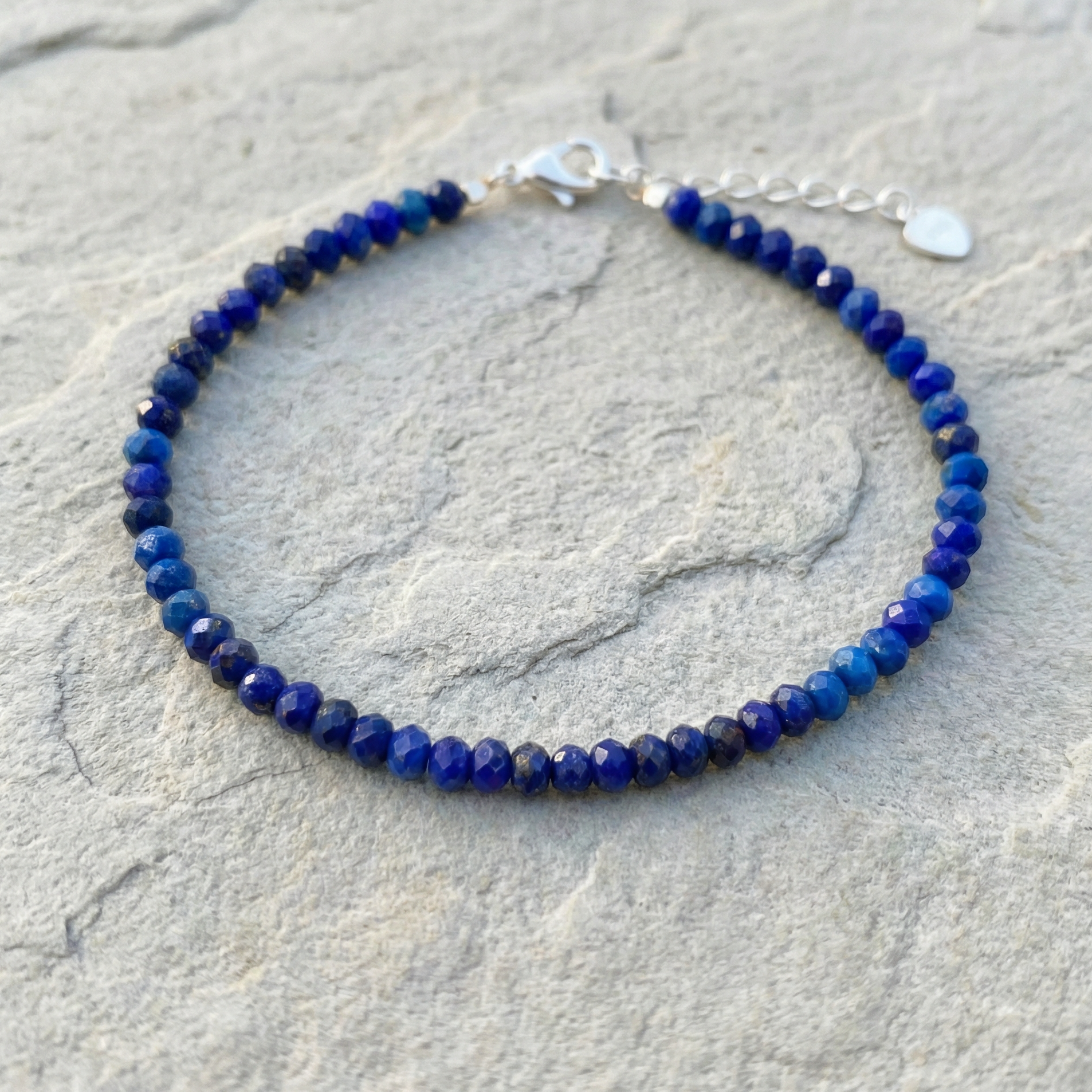 Blue lapis lazuli beaded bracelet with 925 silver clasp on a stone surface