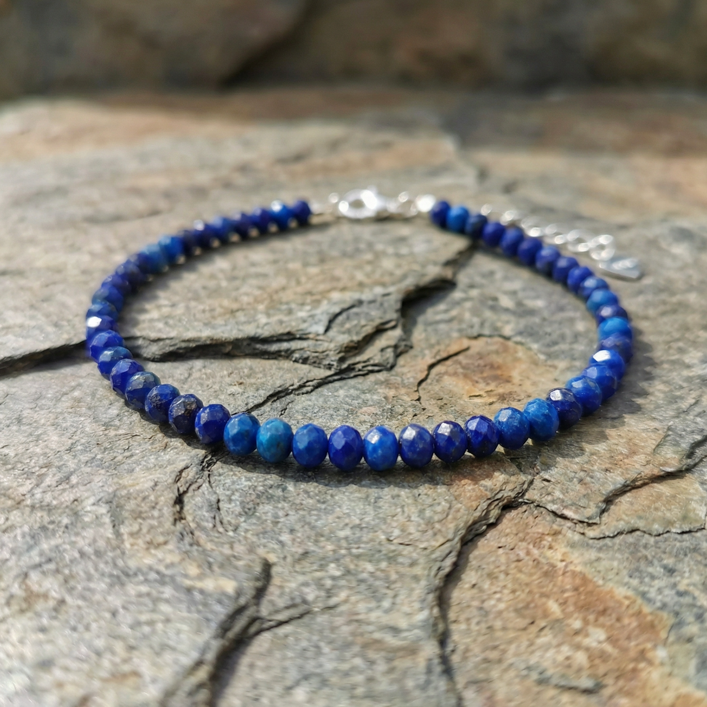 Blue lapis lazuli beaded bracelet with 925 silver clasp on a stone surface