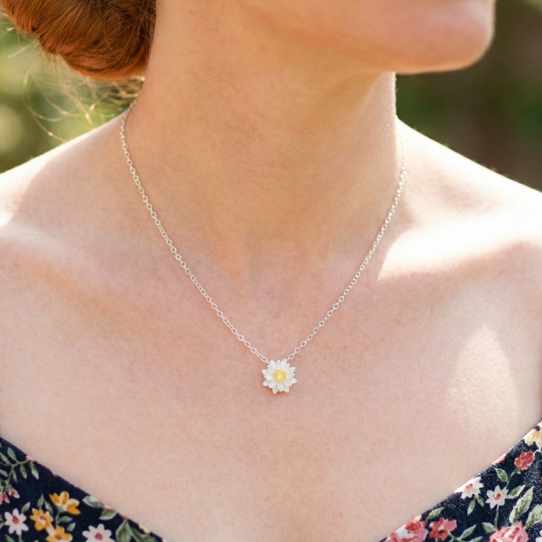 Silver necklace with a daisy pendant worn by a person outdoors