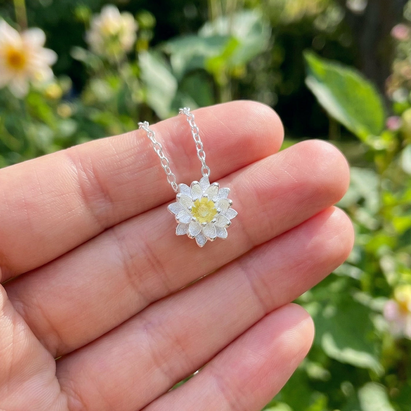 Flower-shaped silver necklace held in a hand with a natural background