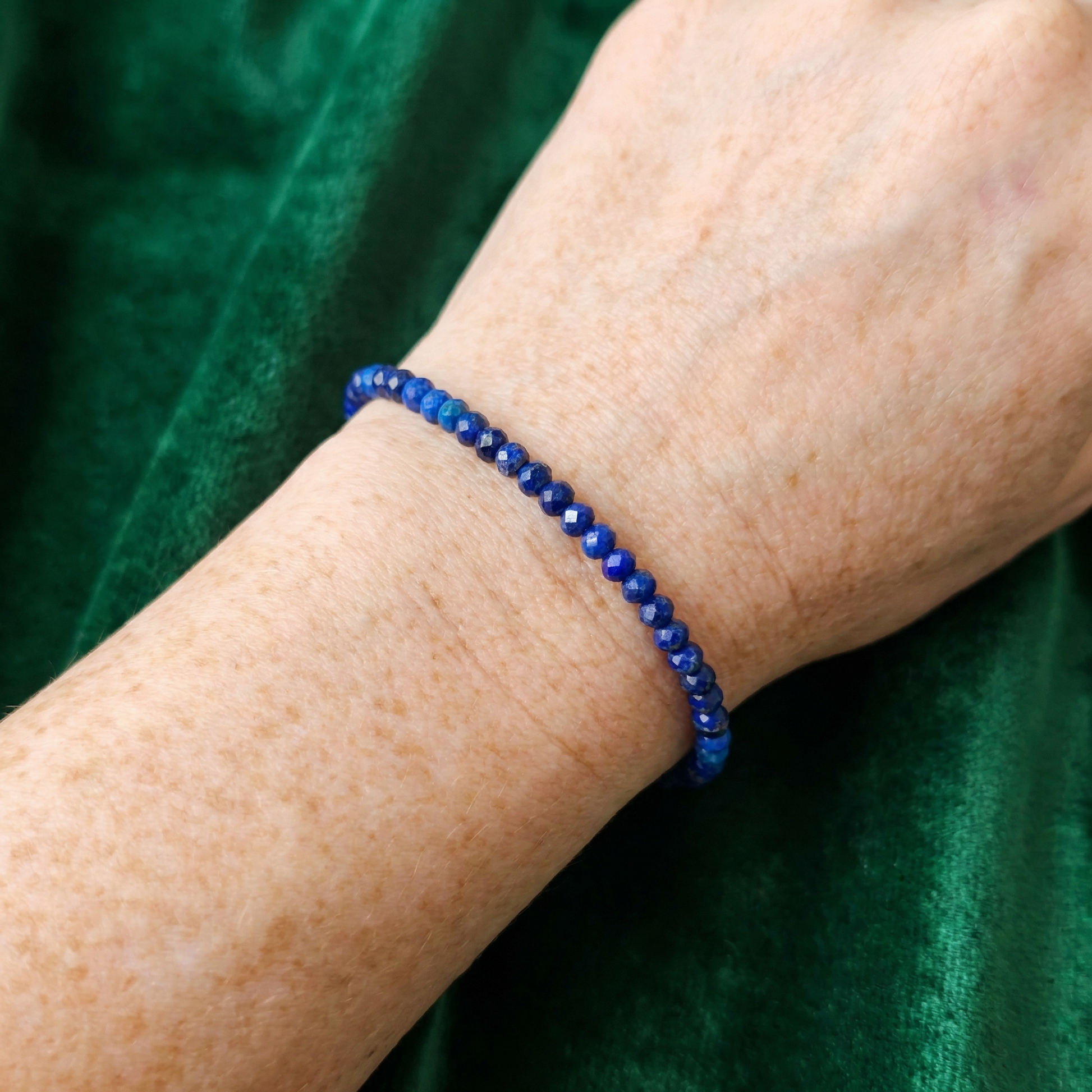 Blue lapis lazuli beaded bracelet on a wrist against a green background