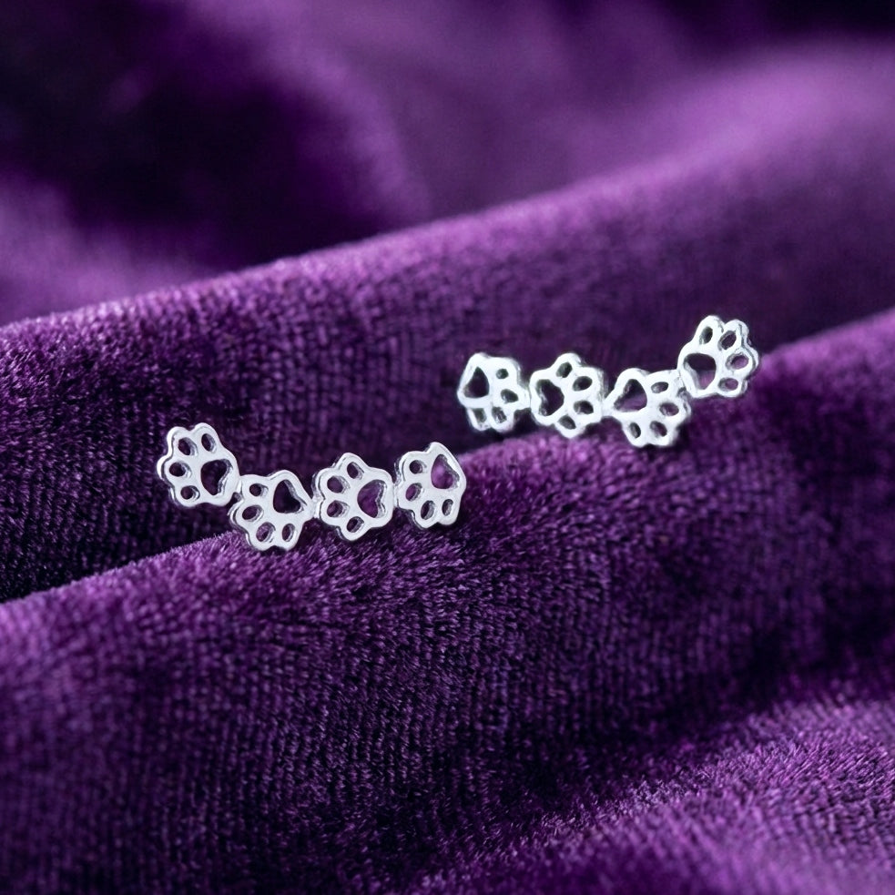 Silver dog paw print earrings on a purple fabric background