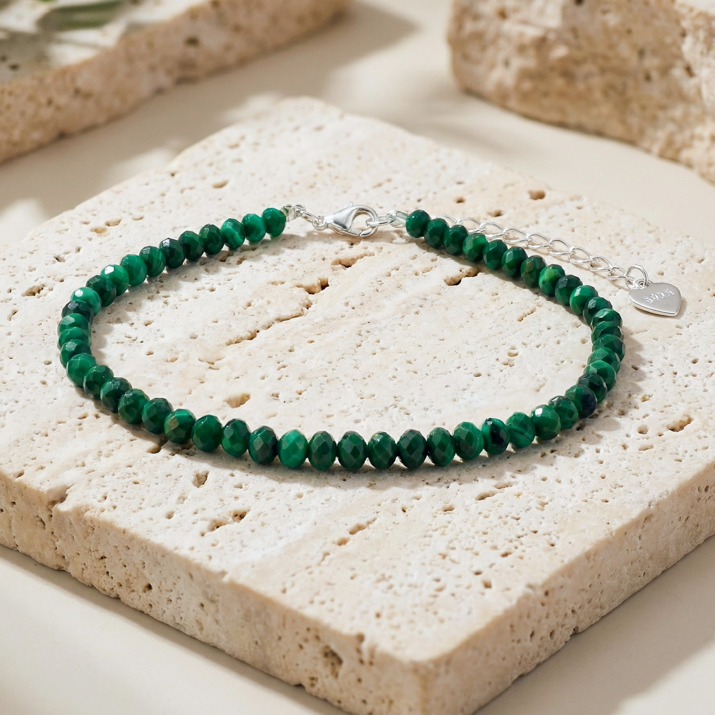 Natural green malachite bead bracelet with a 925 silver clasp on a light stone background