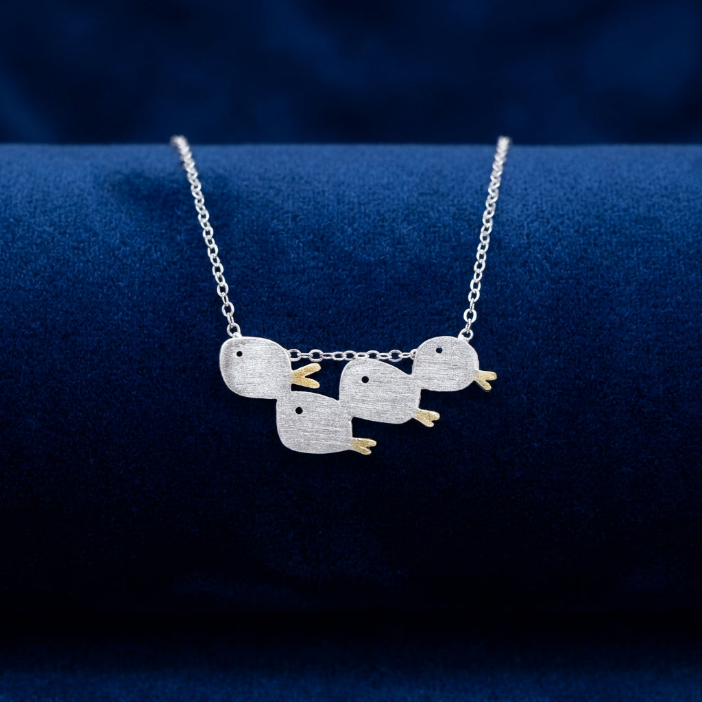 Matte brushed silver necklace with a school of four fishes with gold tails, on a blue fabric background