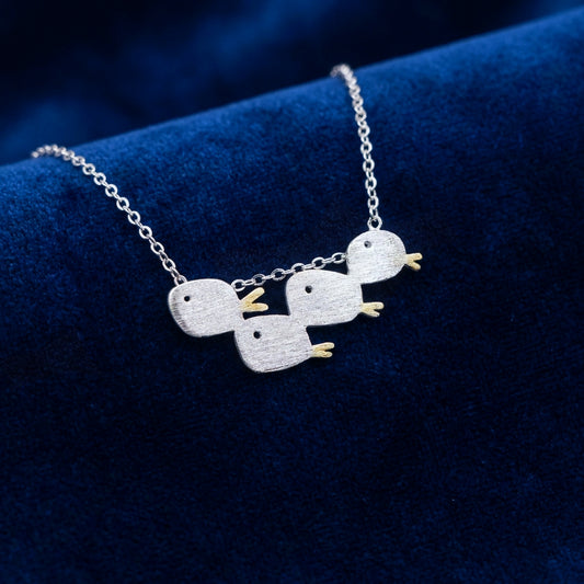 Matte brushed silver necklace with a school of four fishes on a blue fabric background