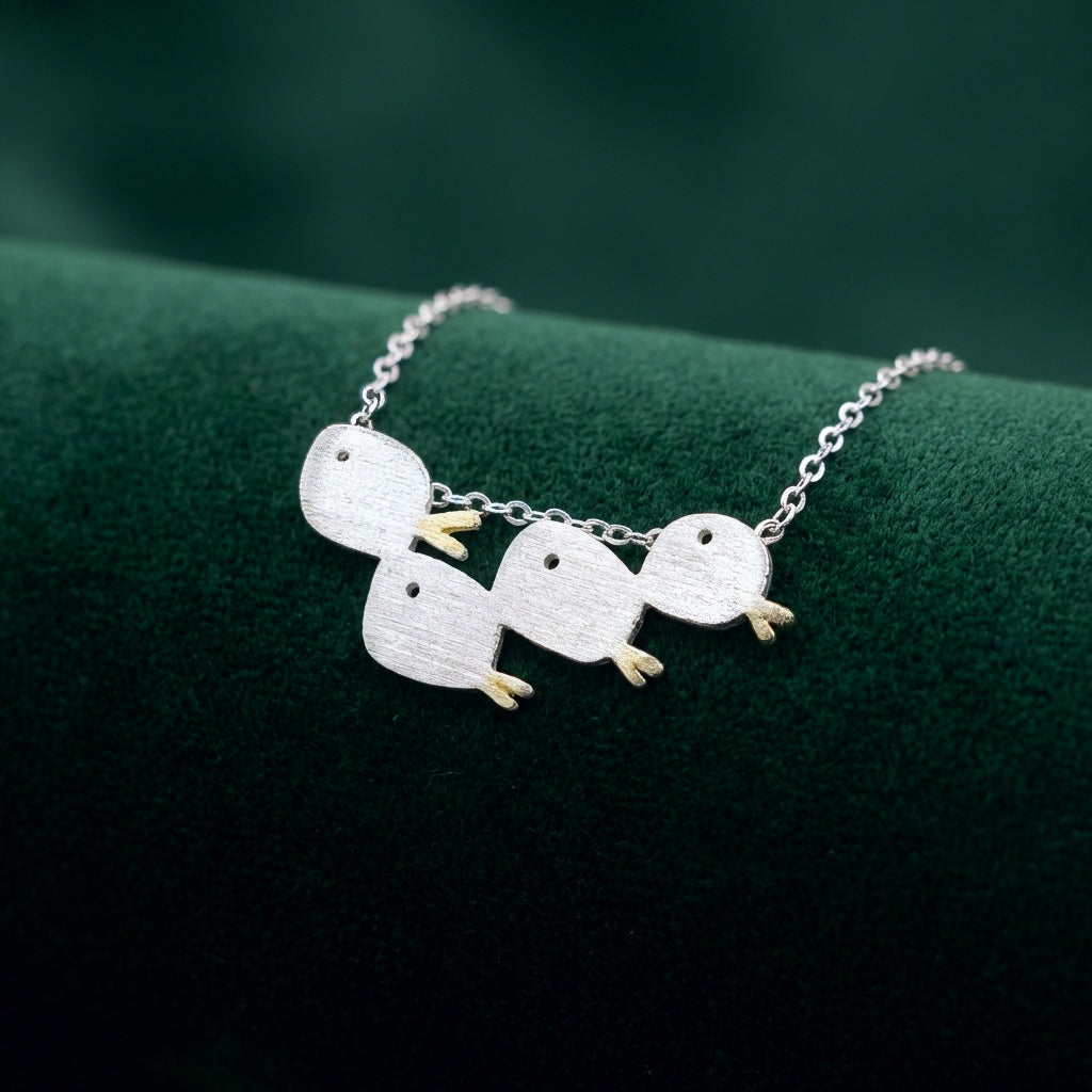 Matte brushed silver necklace with a school of four fishes with gold tails, on a green fabric background